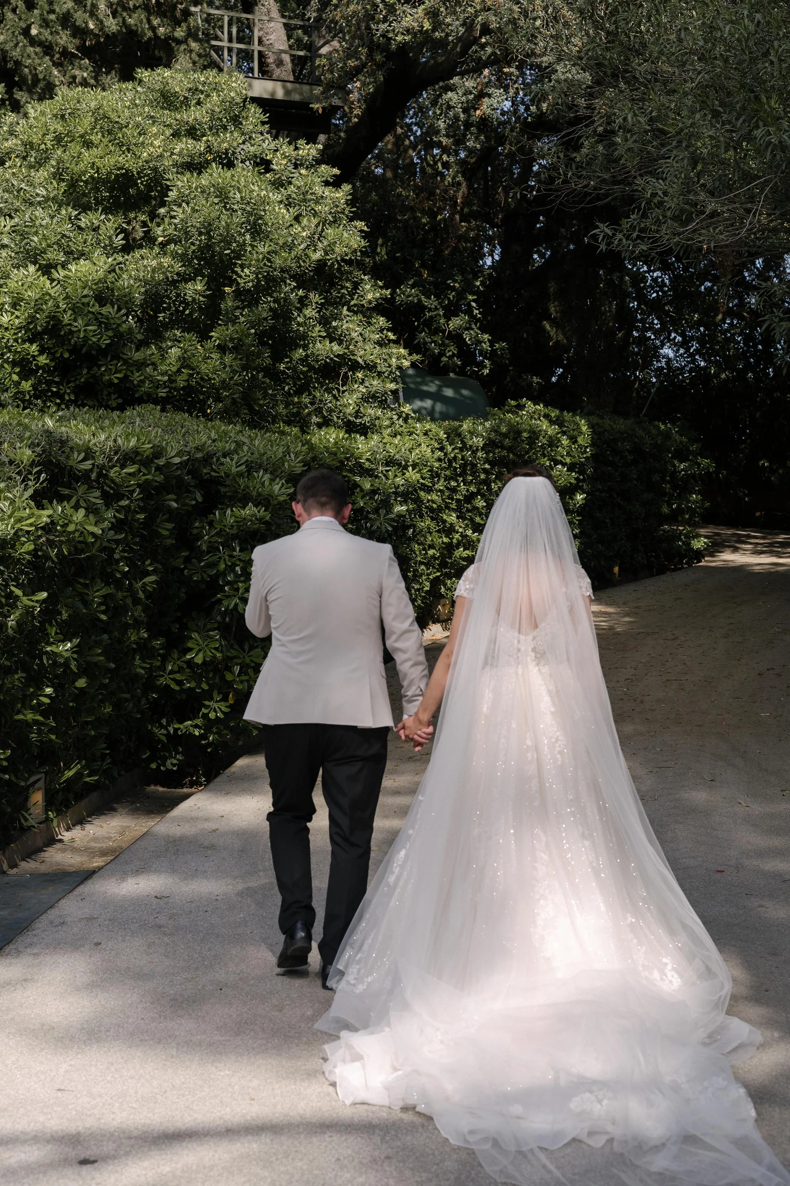 Ellie and Ernie walking together along a garden path, with her veil trailing behind