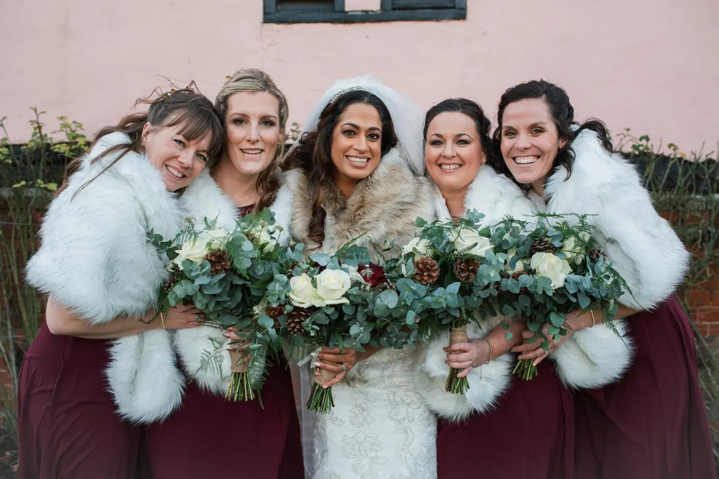 Bridesmaids in faux fur wraps laughing with the bride