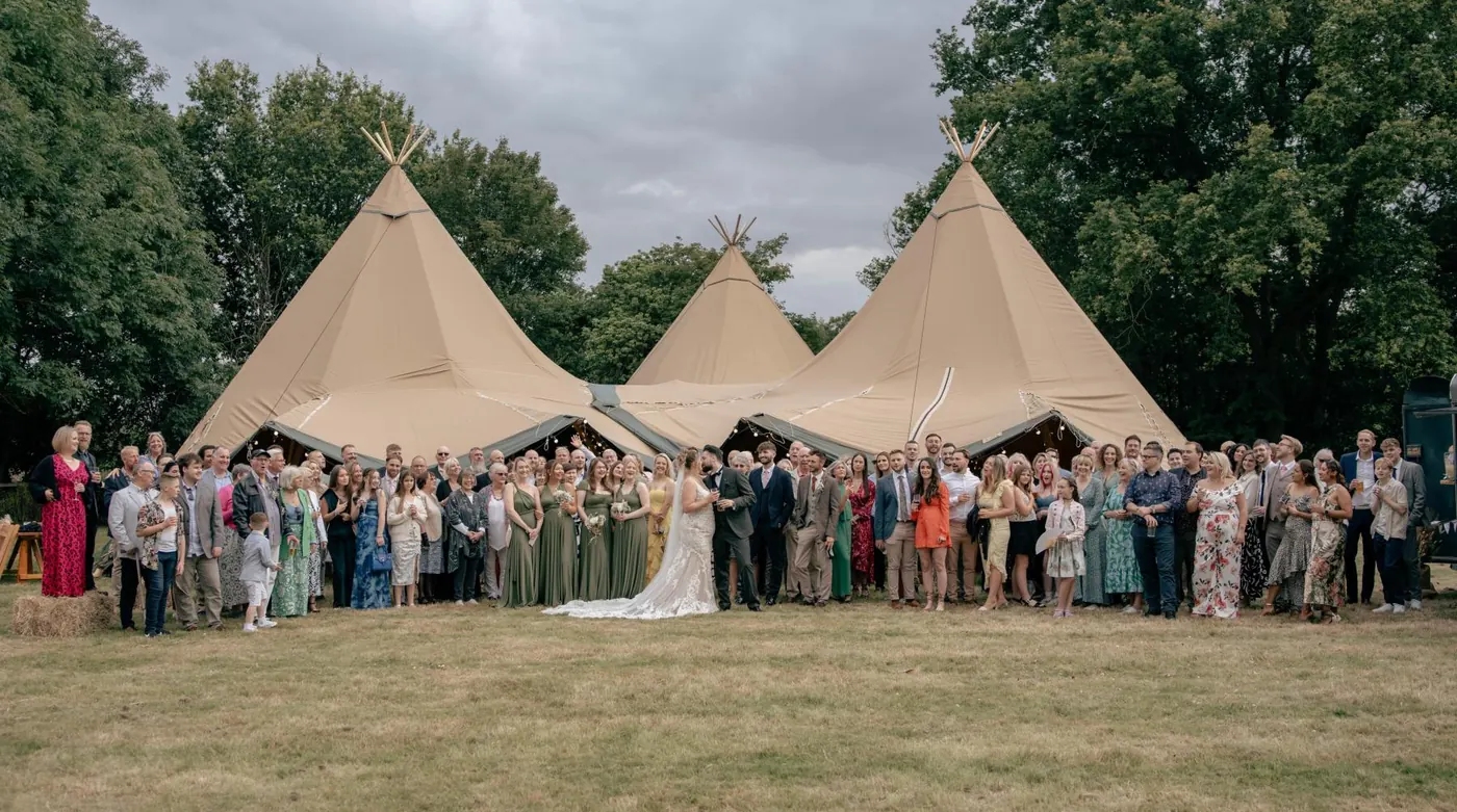 Whole-wedding group photo on the lawn in front of three tipis