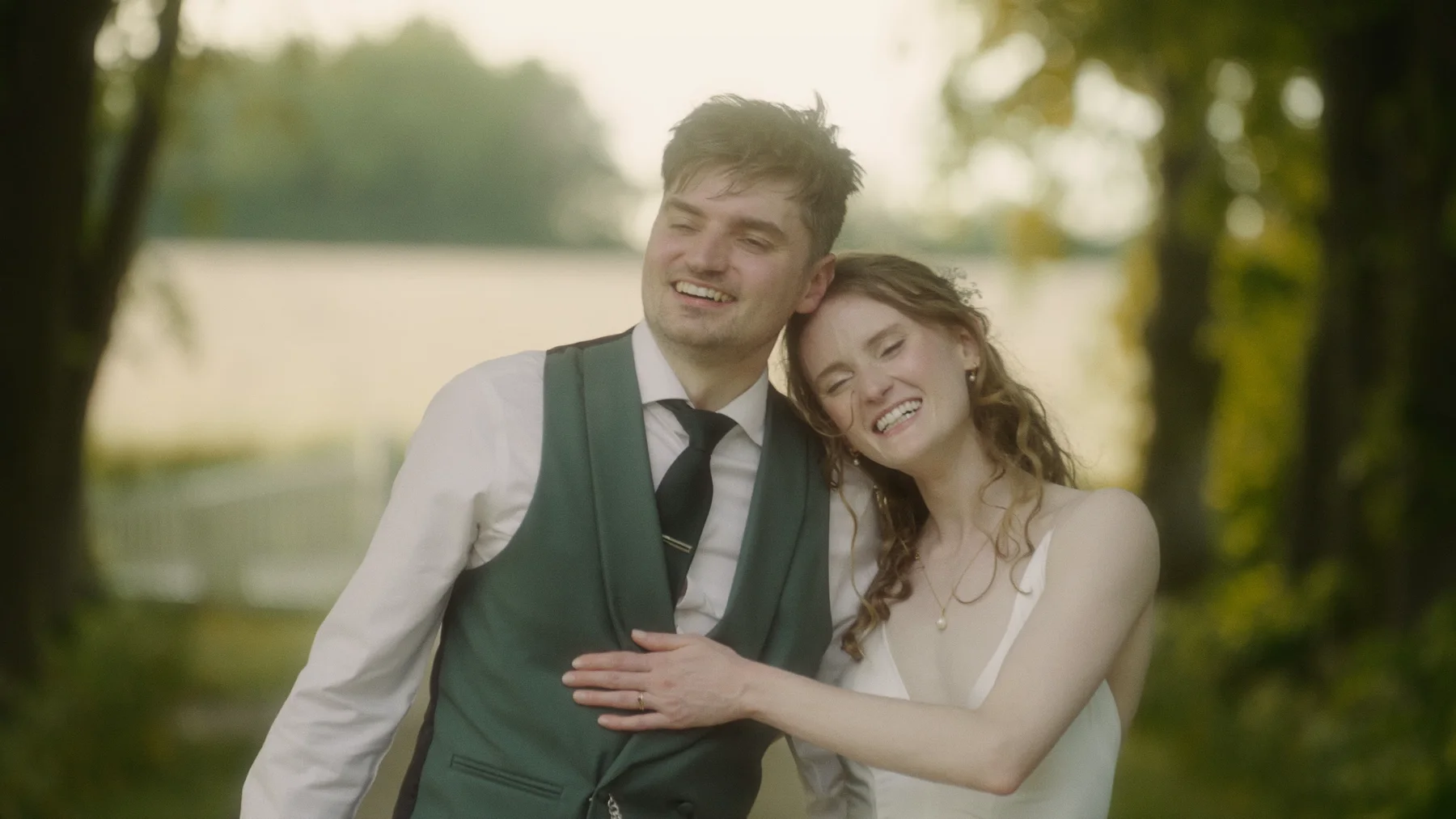 Charlotte resting her head on Dom’s shoulder as they laugh beneath the trees