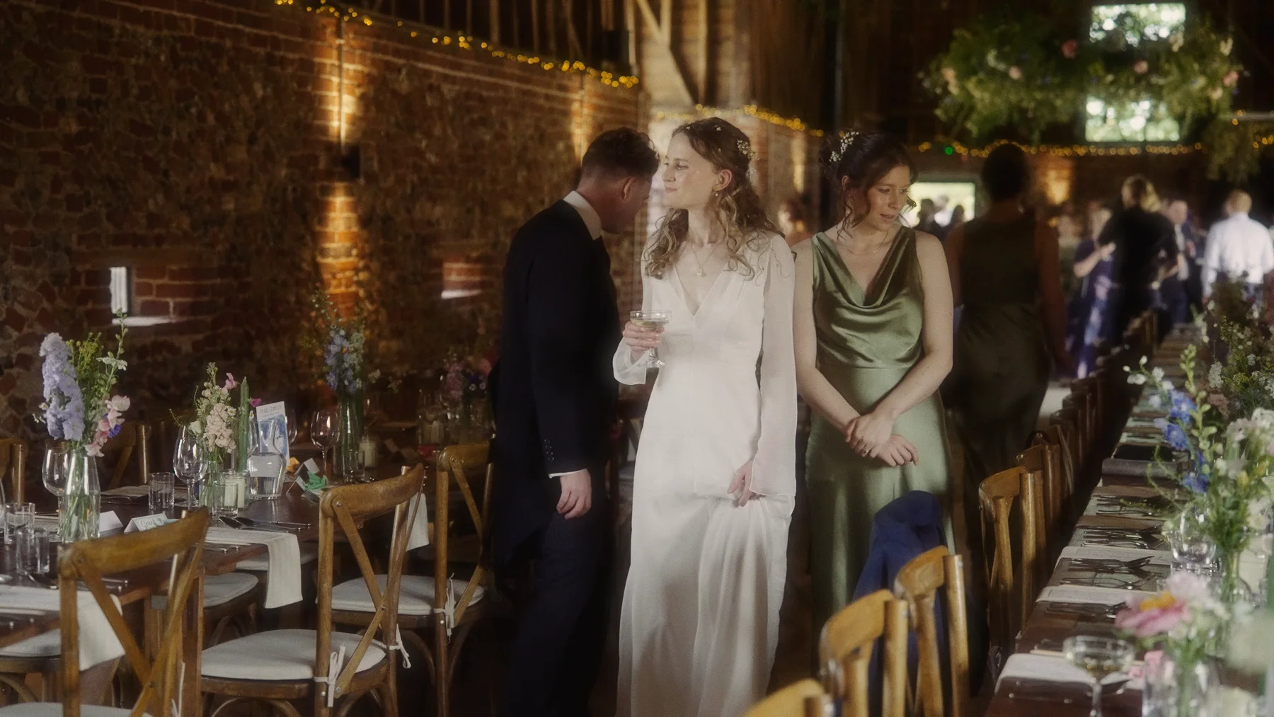 Charlotte and Dom looking along the flower-decorated tables inside the timber-beamed wedding barn