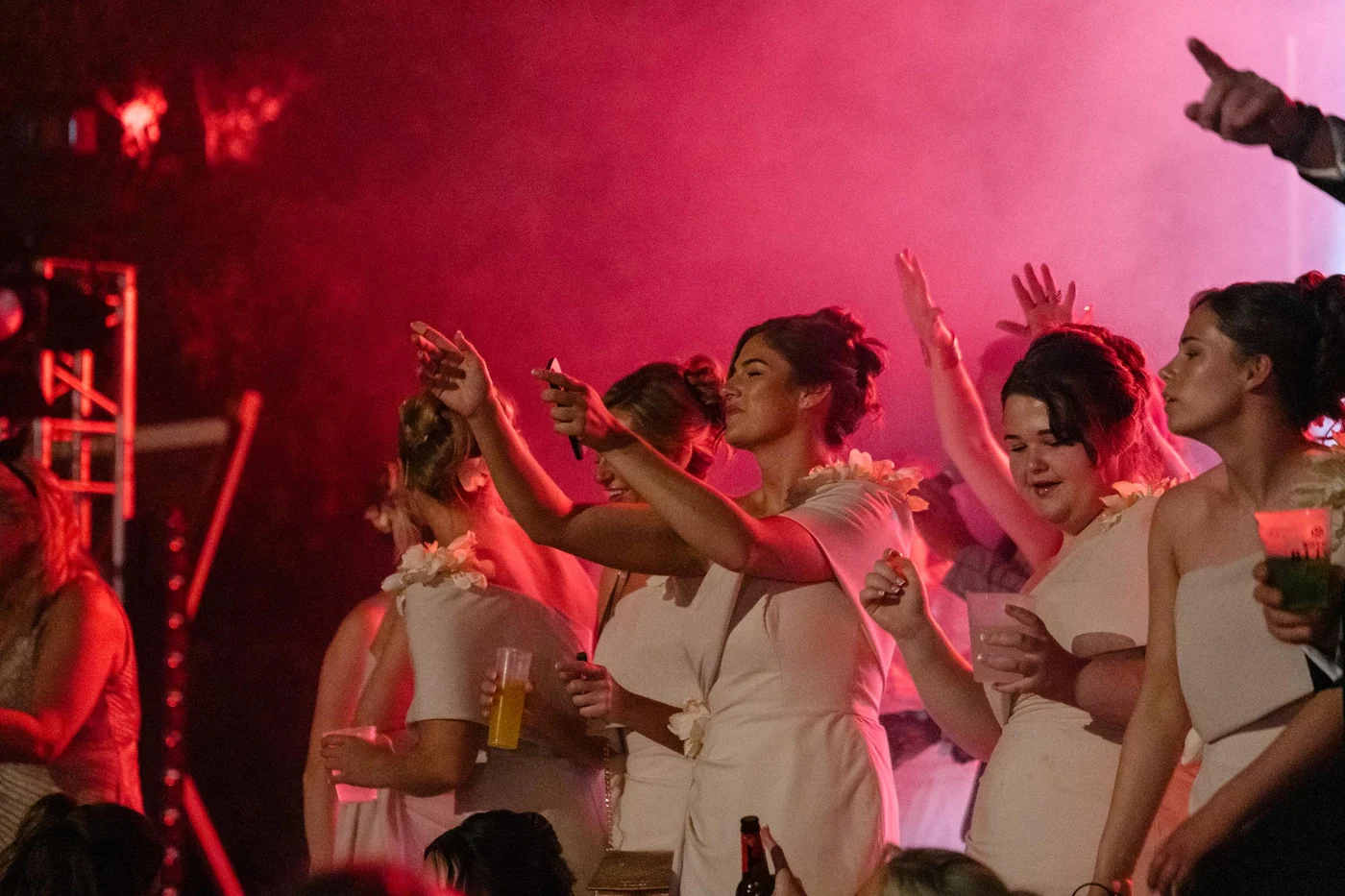 Ellie and her friends dancing with their arms raised beneath pink lights