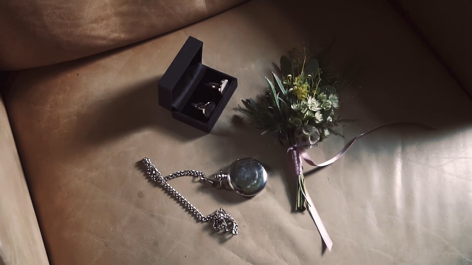 A pocket watch, cufflinks and buttonhole laid out for the groom — film still