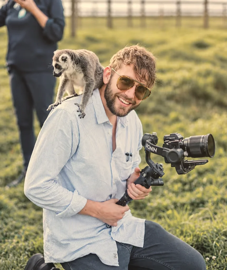 Sam filming at a wedding with his camera gimbal, a ring-tailed lemur perched on his shoulder